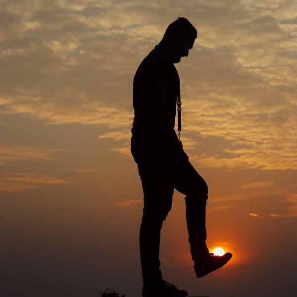 Silhouette of a man in a focused, balanced pose against a dark background with a coral light.